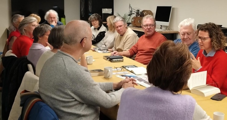 Een groep mensen rond een tafel die een boek bespreken Een groep mensen rond een tafel die een boek bespreken